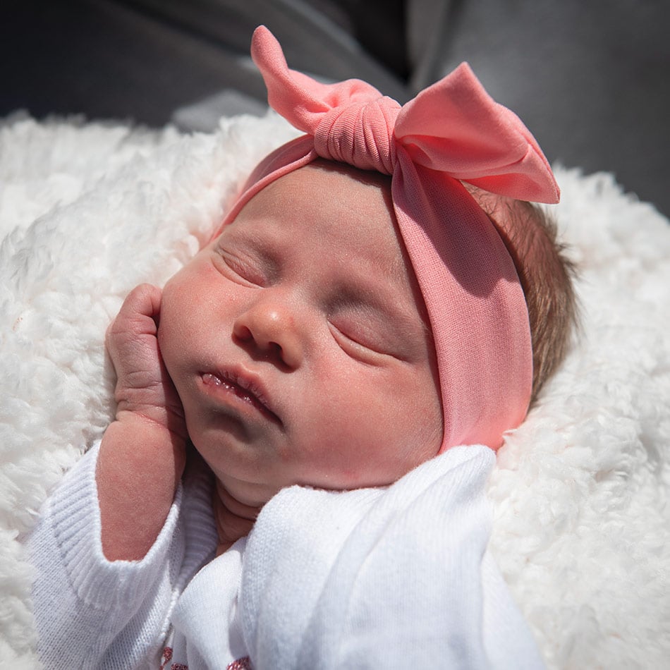 Infant girl with a pint bow and white cushion underneath her