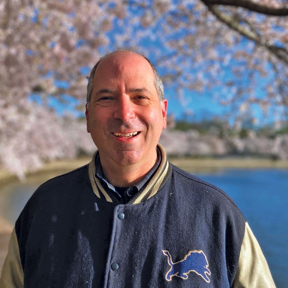 Rob Nosanchuk wearing a letterman jacket, smiling at the camera with pink cherry blossom trees in the background