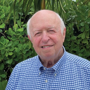 Senior man smiling in front of greenery wearing blue gingham button up shirt