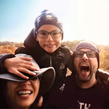 Man woman boy wearing glasses and hats outside on clear day colorful trees in background 