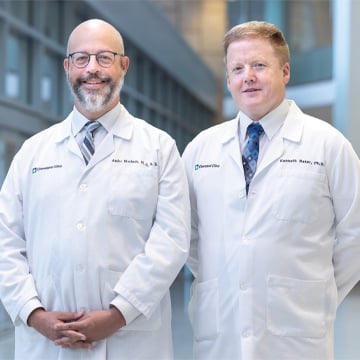 Bald male doctor glasses striped tie lab coat standing next to male doctor strawberry blonde hair blue patterned tie lab coat