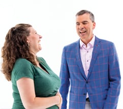 Woman green top curly brown hair man blue suit jacket with red stripes lavender shirt both laughing