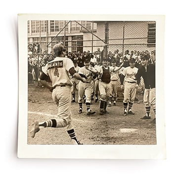 Black and white photo of baseball player running to home plate and team waiting to congratulate him