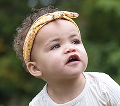 Baby girl curly brown hair headband crawling on grassy lawn