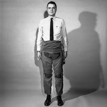 black and white image of a man wearing a white shirt and black tie, in baggy pants