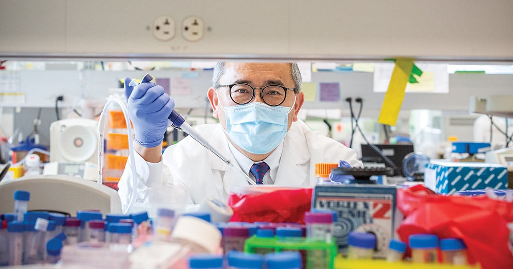 doctor with face mask on, holding medical tool, looking ta camera through shelves