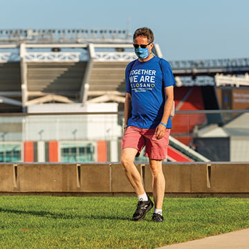 Man wearing blue VeloSano shirt, a face mask and pink shorts, walking outside of First Energy stadium