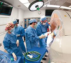 A group of doctors wearing medical/surgical gowns and PPE, performing a procedure with a large white machine
