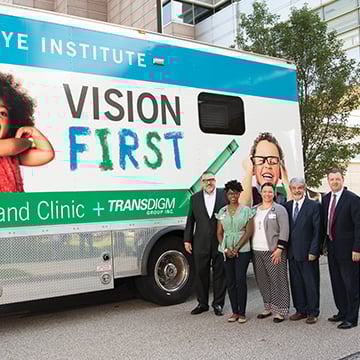 3 men and 2 women standing outside in front of a bus with the words