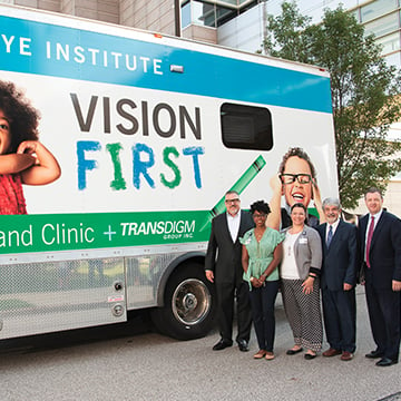 3 men and 2 women standing outside in front of a bus with the words 