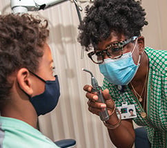 A female doctor wearing a green shirt and glasses, checks the eyesight of a child
