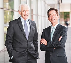 Larry Pollock & Stewart Kohl wearing business attire, standing in front of a building outside, smiling at camera.