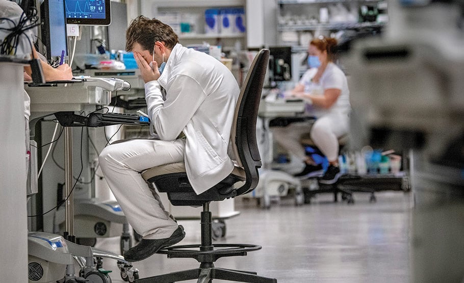 An exhausted doctor sitting at computer with his face in his hands