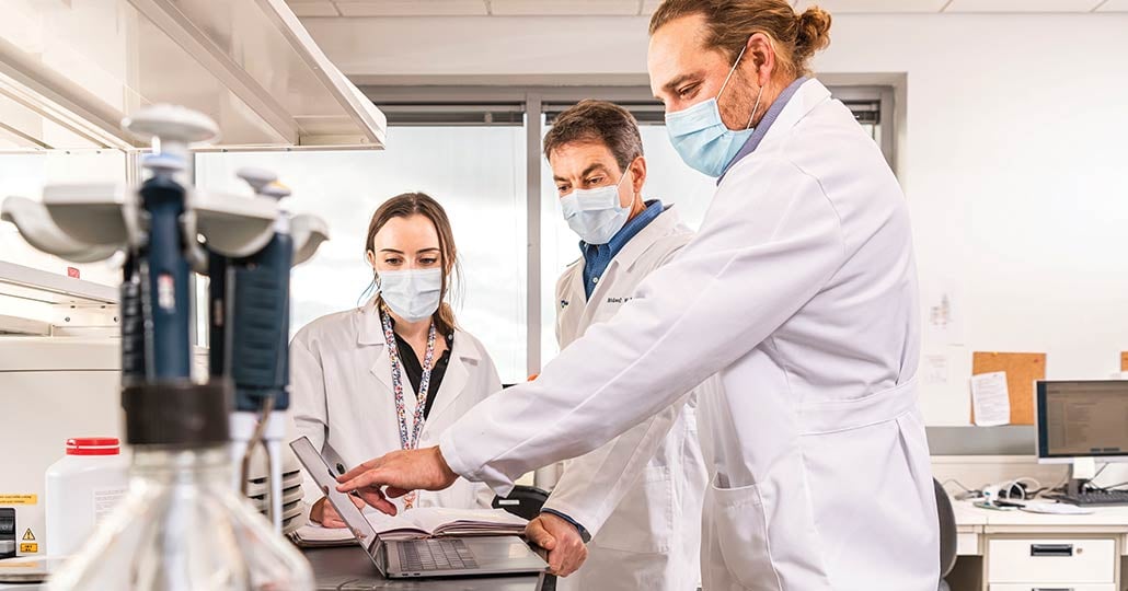 Three doctors looking at a laptop in a science lab