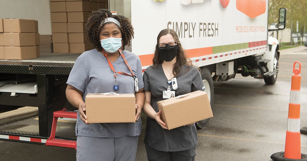 Two female doctors wearing face masks, standing outside holding packages