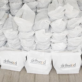 Stacks of white takeout bags with a driftwood logo printed on front