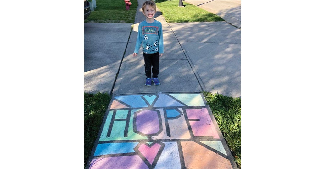 Young Boy standing in front of chalk drawing that says hope