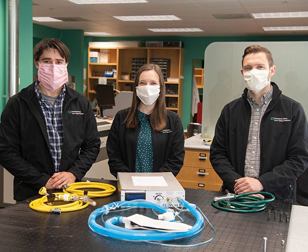 three students stand behind a table wearing face masks