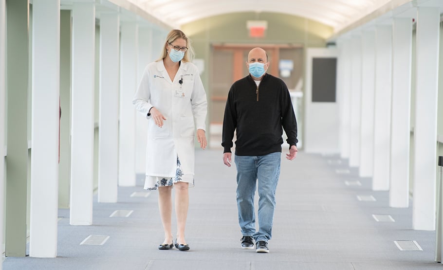 A female doctors and a male patient wearing surgical face masks, walking in a corridor