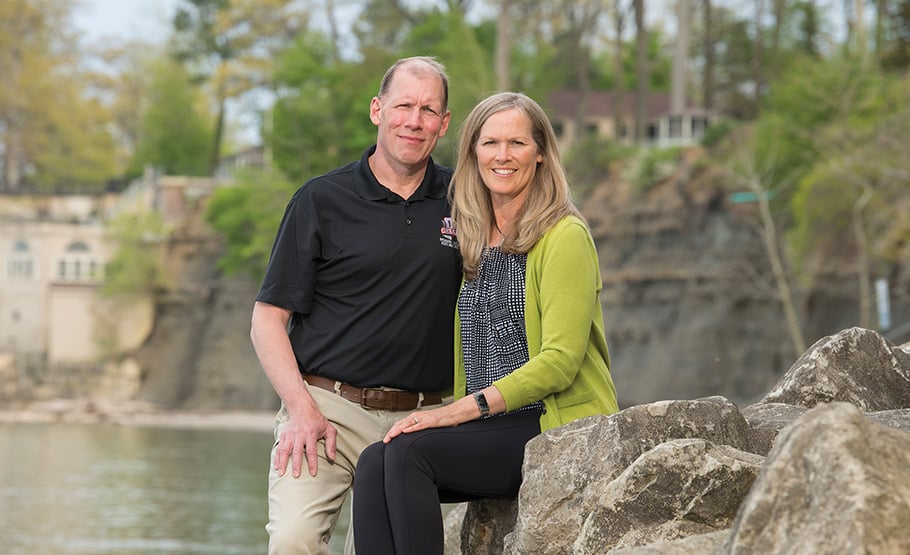 Kevin Kelley and his wife posing for a photo on a rock with a pond behind them