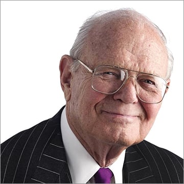 David T. Morgenthaler smiling, wearing wide eyeglasses and a pinstriped suit. Posing for a photo in front of a white background