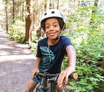 A young boy wearing a helmet on a bike in the woods