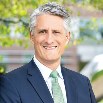 Headshot of man outside wearing blue suit jacket with green tie and white shirt