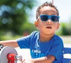 Young black boy on tricycle wearing blue t-shirt and sunglasses